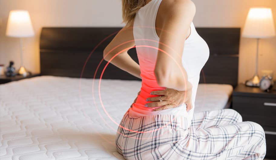 Dame zittend op bed met rugpijn